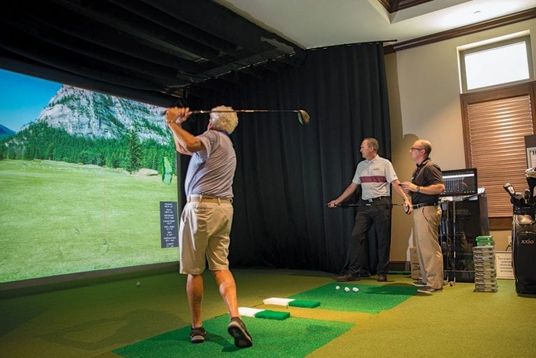 Golfer swinging club on Boca West's golf simulator during instruction with the PGA Pro