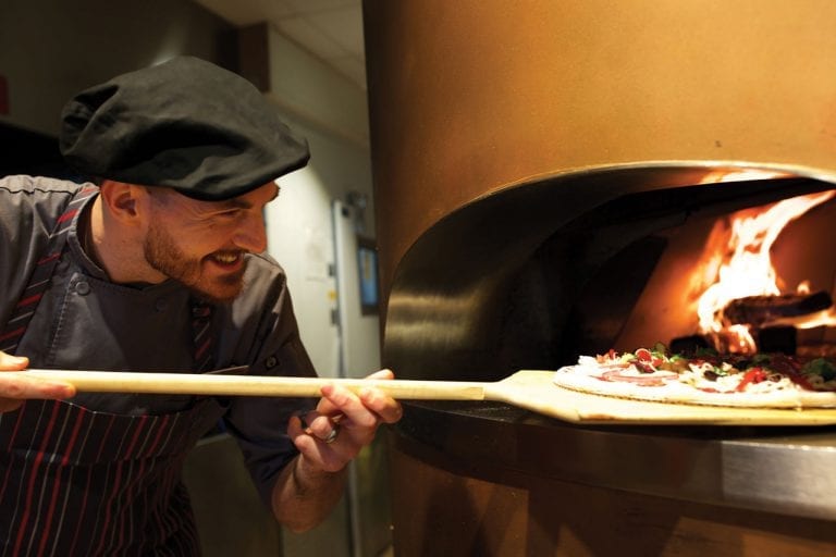 Chef putting pizza in wood fired pizza oven at Boca West's MyPi restaurant